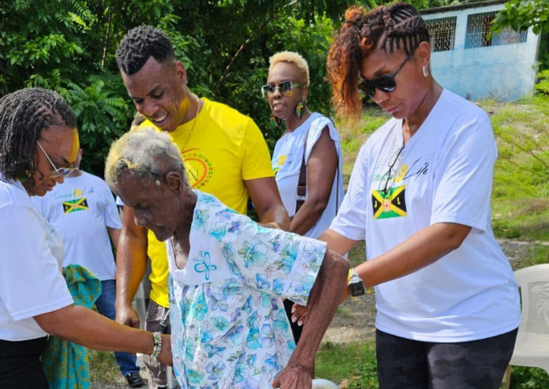 People assisting an elderly woman outdoors.