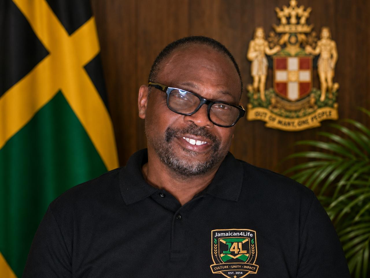 Man smiling in front of Jamaican flag.