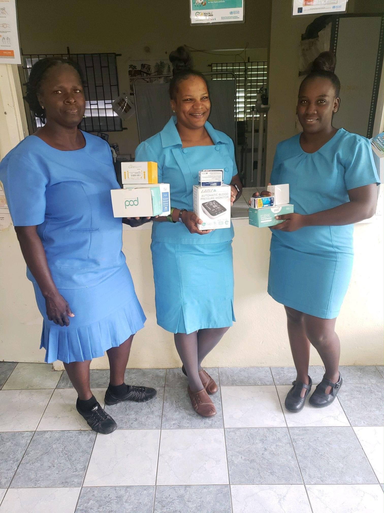 Three women in blue uniforms holding medical supplies